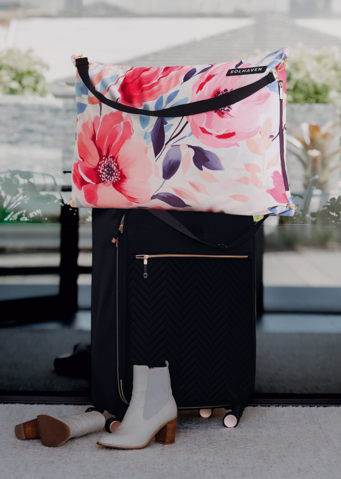 Floral-patterned dream first pillow bag bag on top of a black suitcase with white boots in front