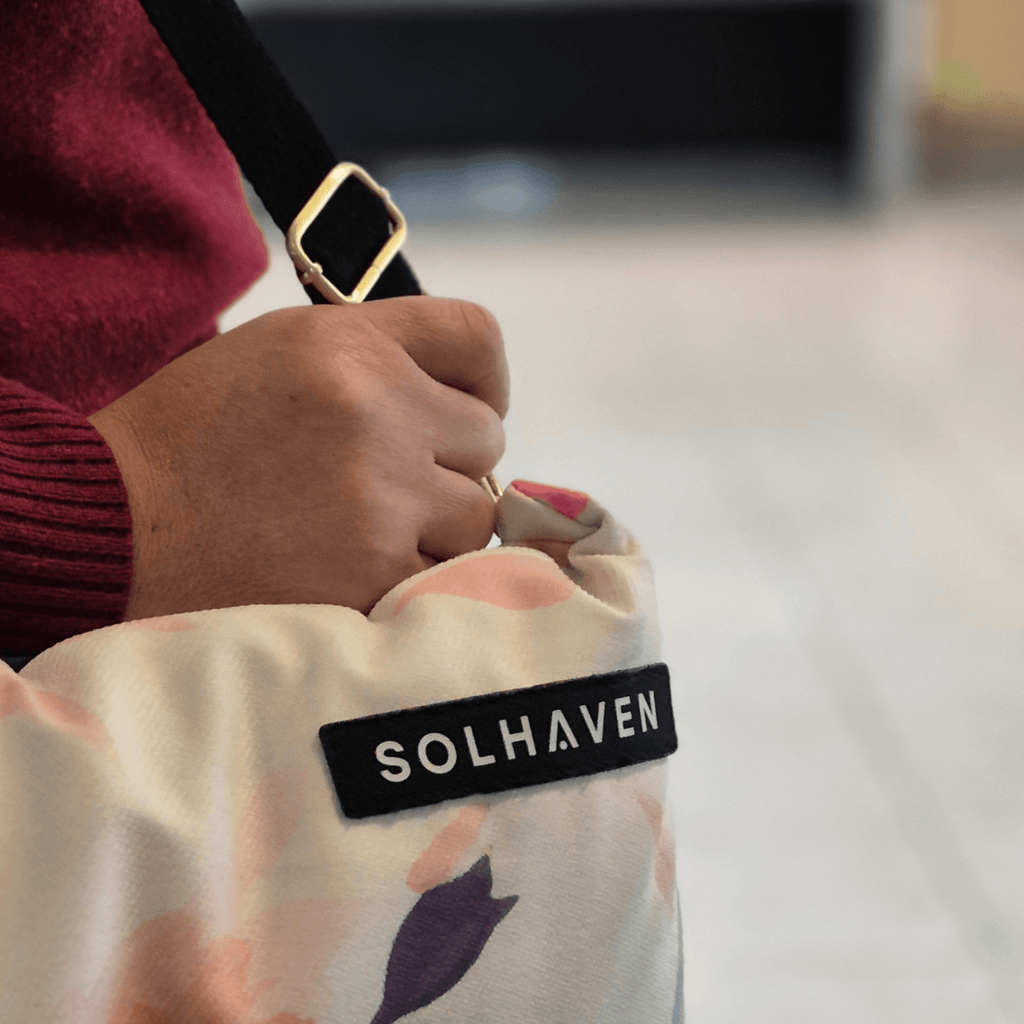 Dream First™ Pillow Bag - Flora - Solhaven, a womans hand holding the bottom of a strap 