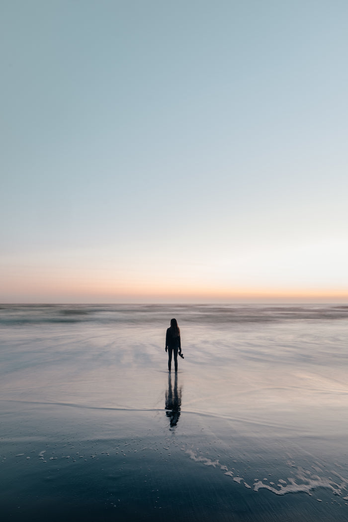 woman standing near ocean at sunset